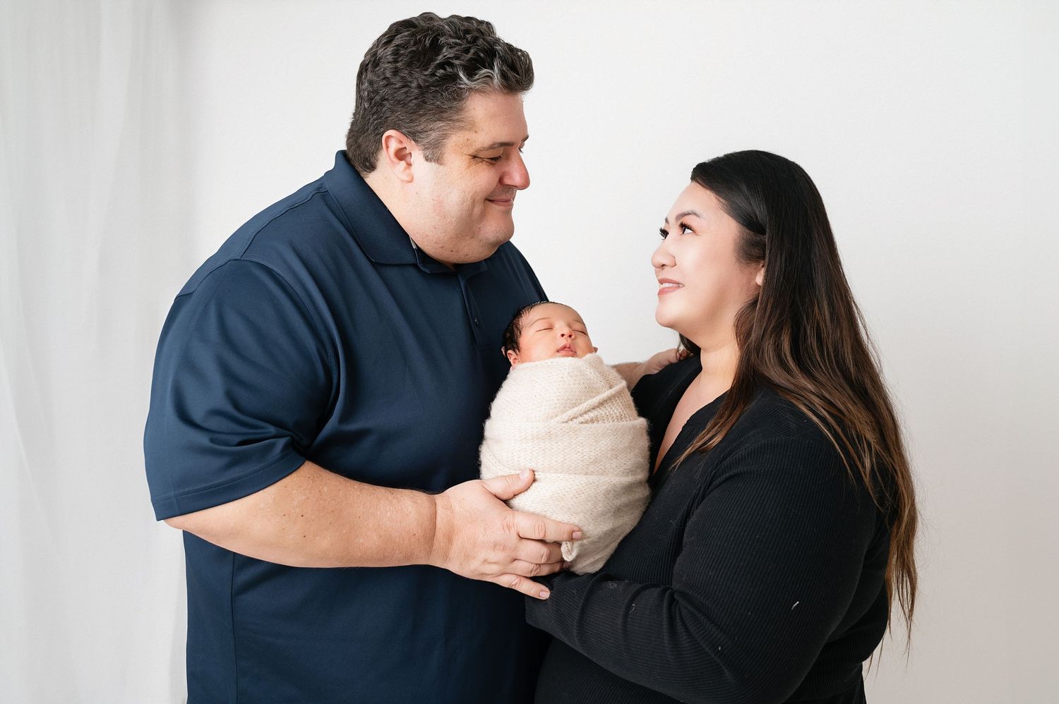 Parents sharing joyful moment with their swaddled newborn during studio photography session.