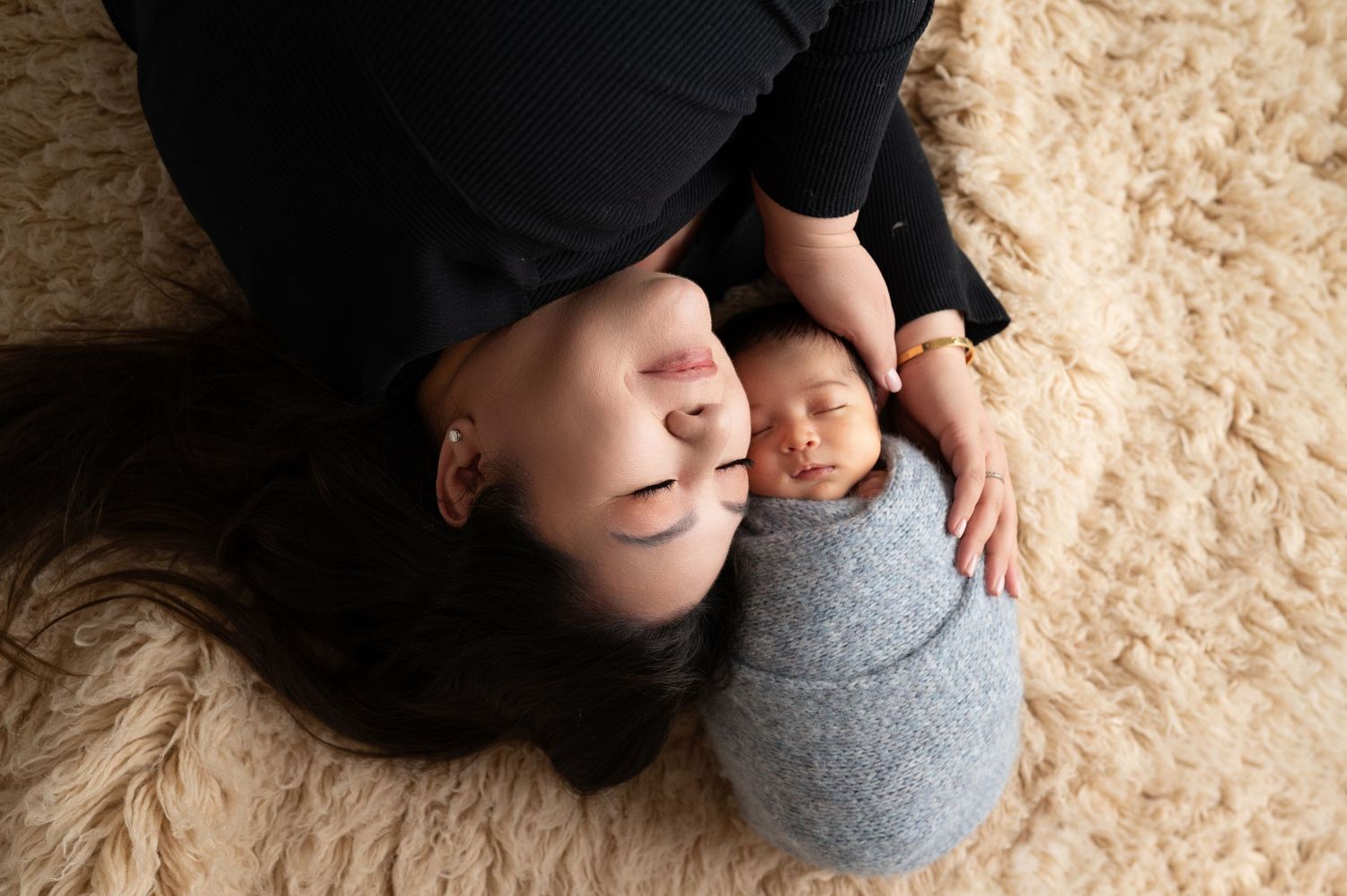Overhead view of parent and newborn lying on textured carpet during intimate photo session.