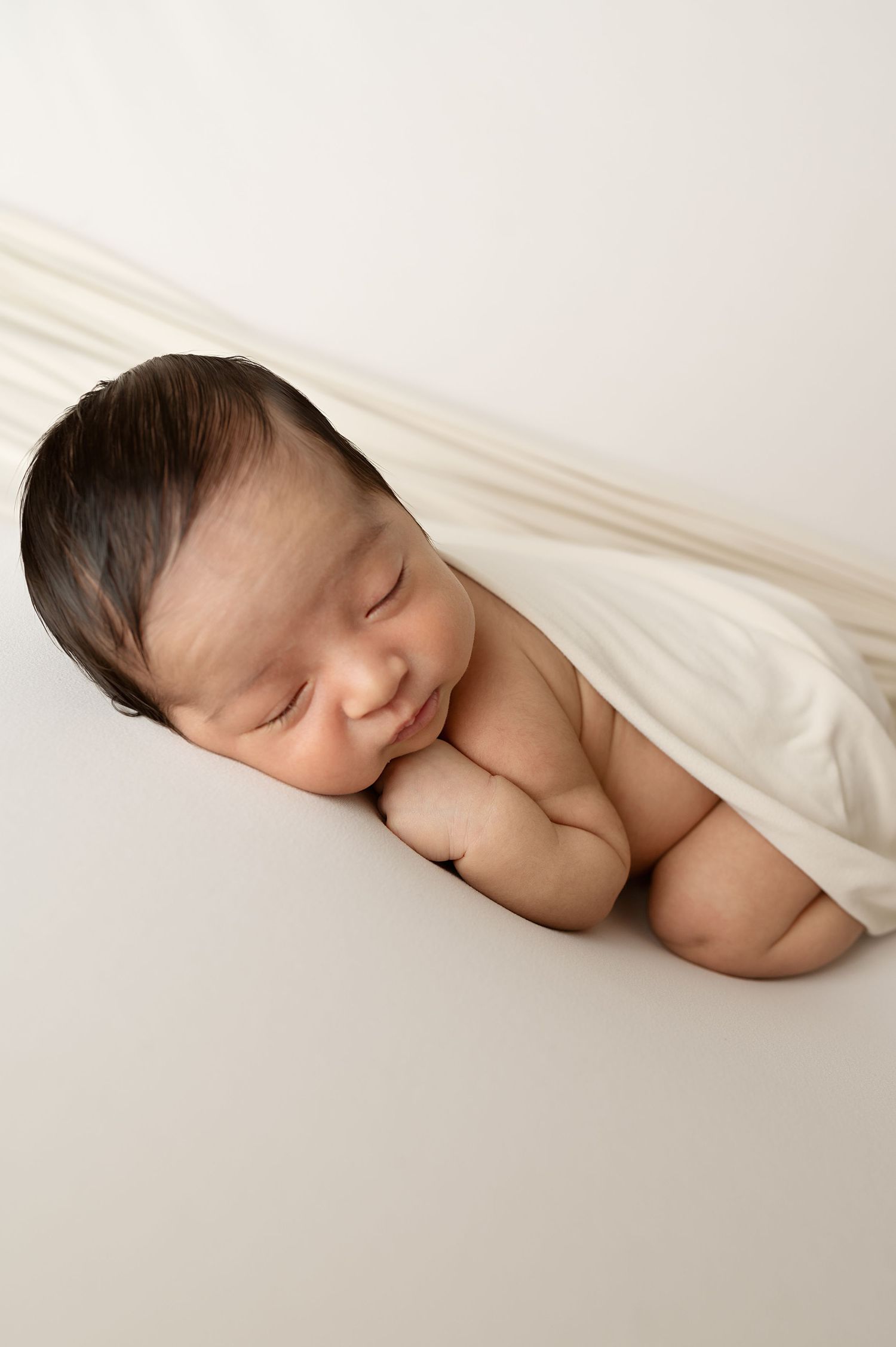 Peaceful sleeping newborn baby wrapped in white blanket during professional photoshoot.
