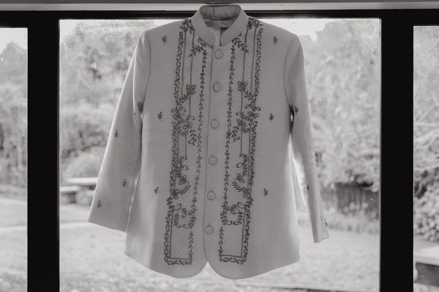 A vintage white shirt with intricate embroidered details hanging against a window.