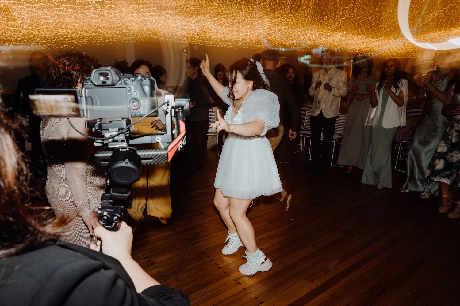 Videographer filming dancers at an indoor celebration event.