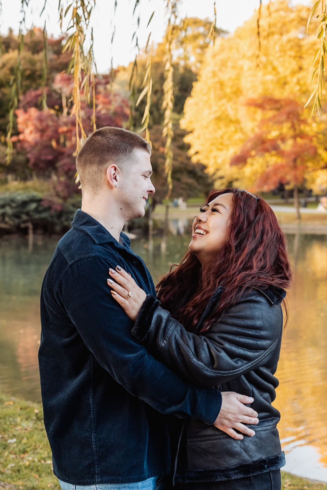 Couple embracing by lake with fall foliage in background.