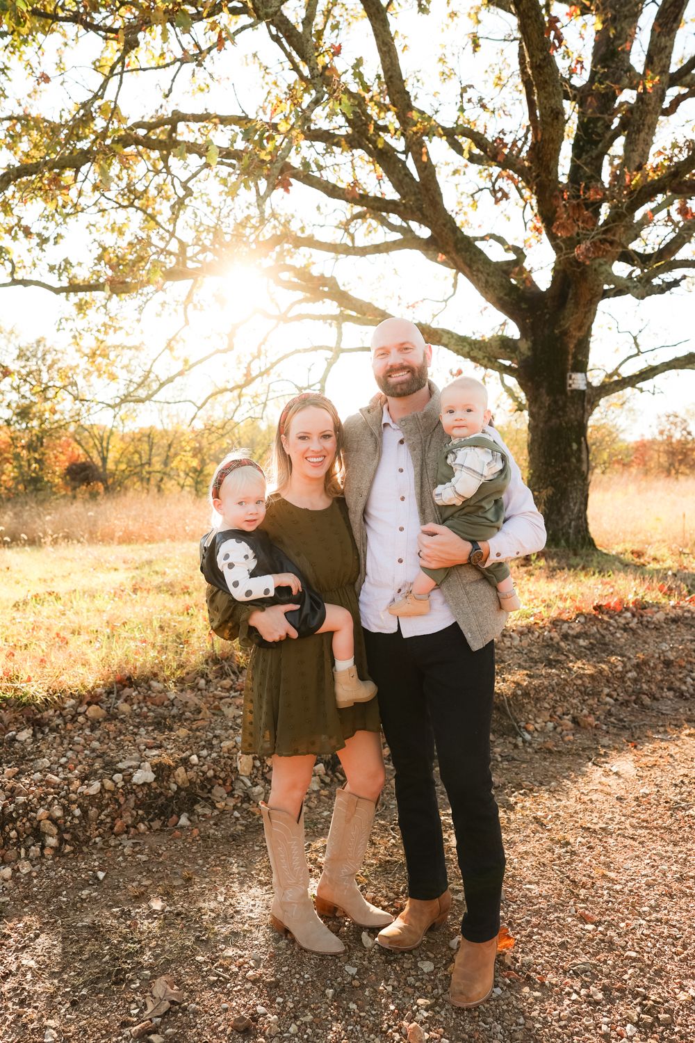 Family poses together under autumn tree with golden sunlight streaming through branches in outdoor portrait session.