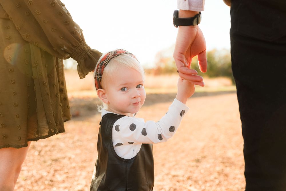 Small child in polka dot outfit reaches up during golden hour photo session outdoors.