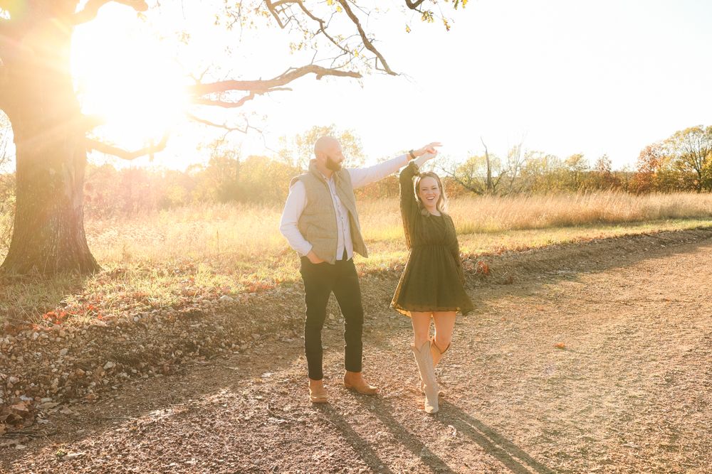 Couple dances together on dirt path during sunset with tree silhouetted in background.