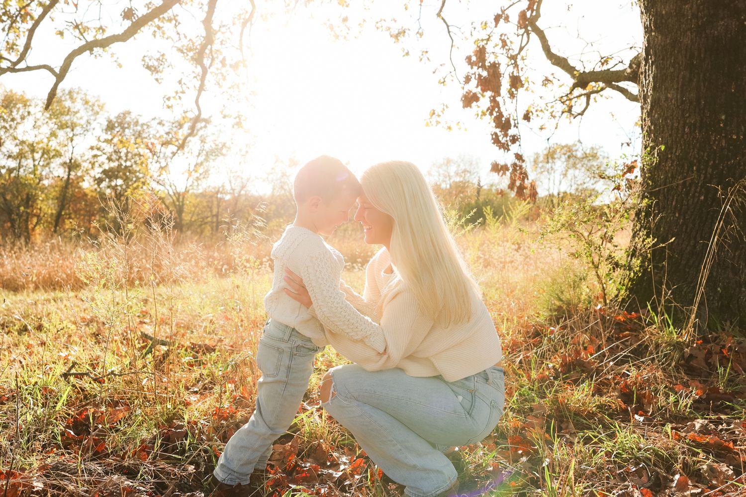 Mother and son share a tender moment under a tree during golden hour sunset.