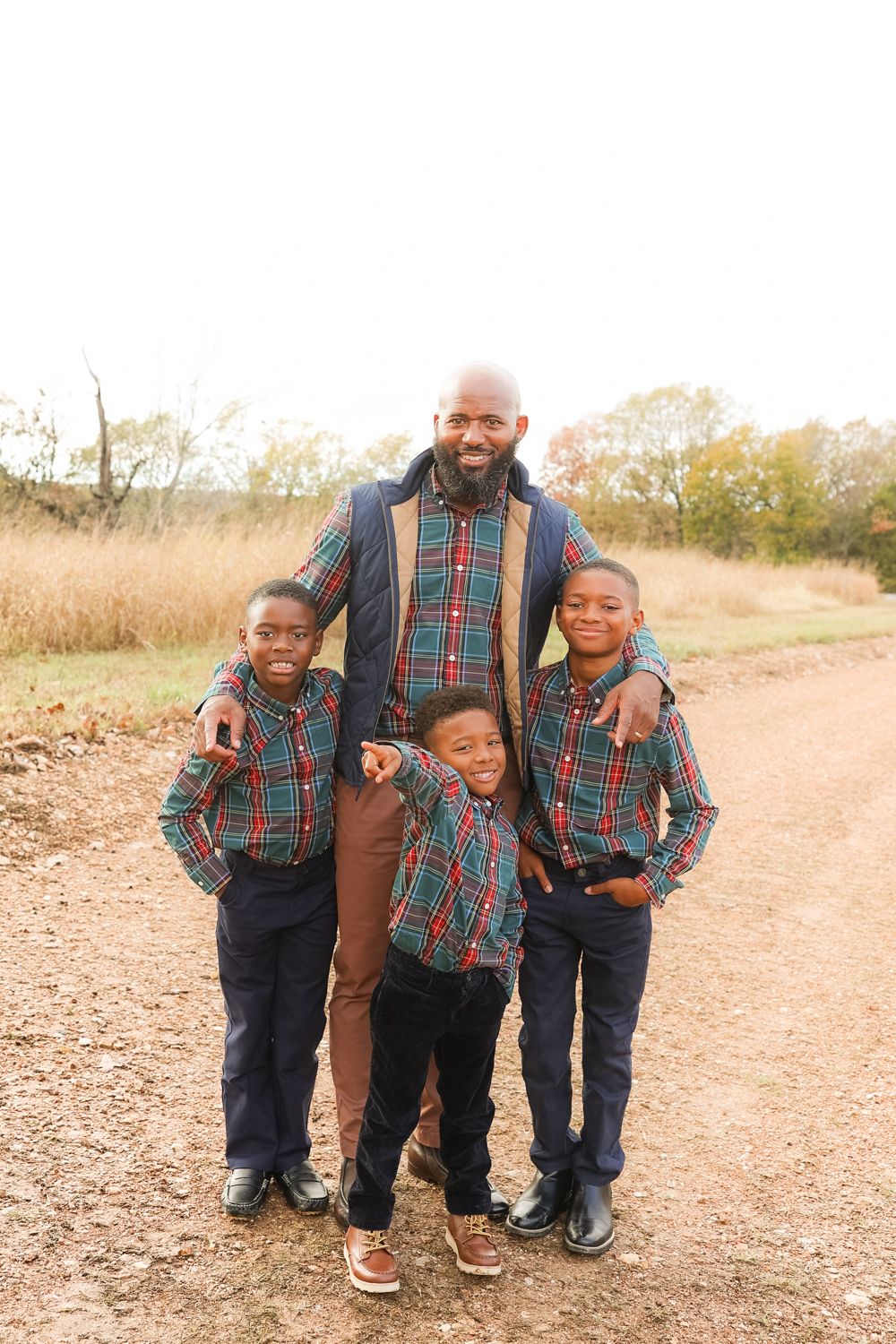 Dad and his son's wearing coordinating plaid outfits poses together on rustic dirt path during autumn photo session.