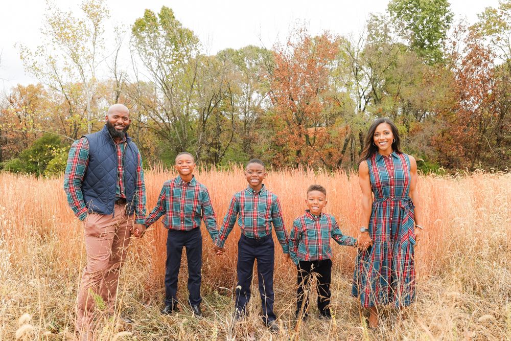 Family stands together in tall autumn grass during outdoor portrait session.