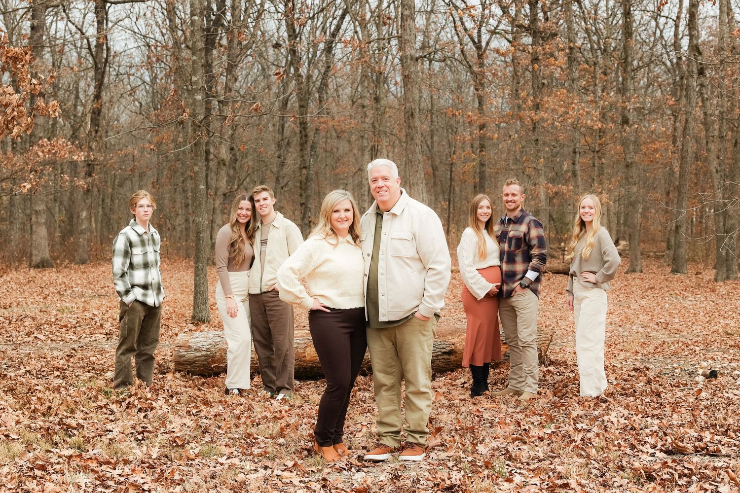 Family group photo session in autumn woods with fallen leaves covering ground.