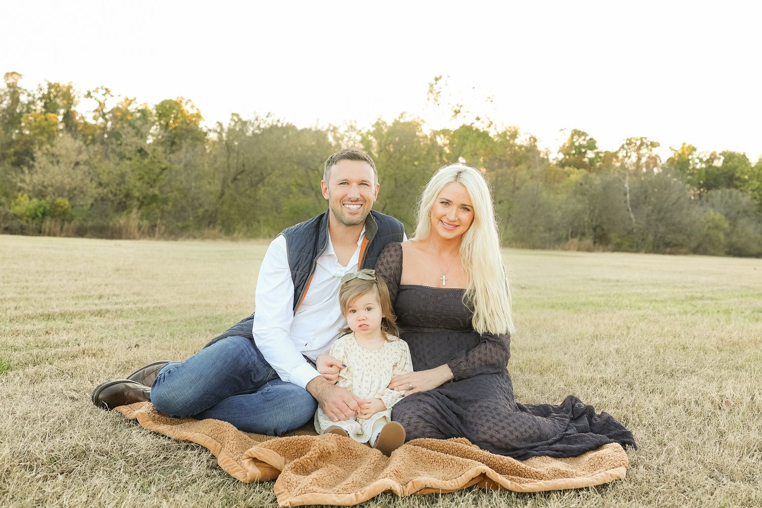 A family sits together on a blanket in a sunlit field during golden hour.