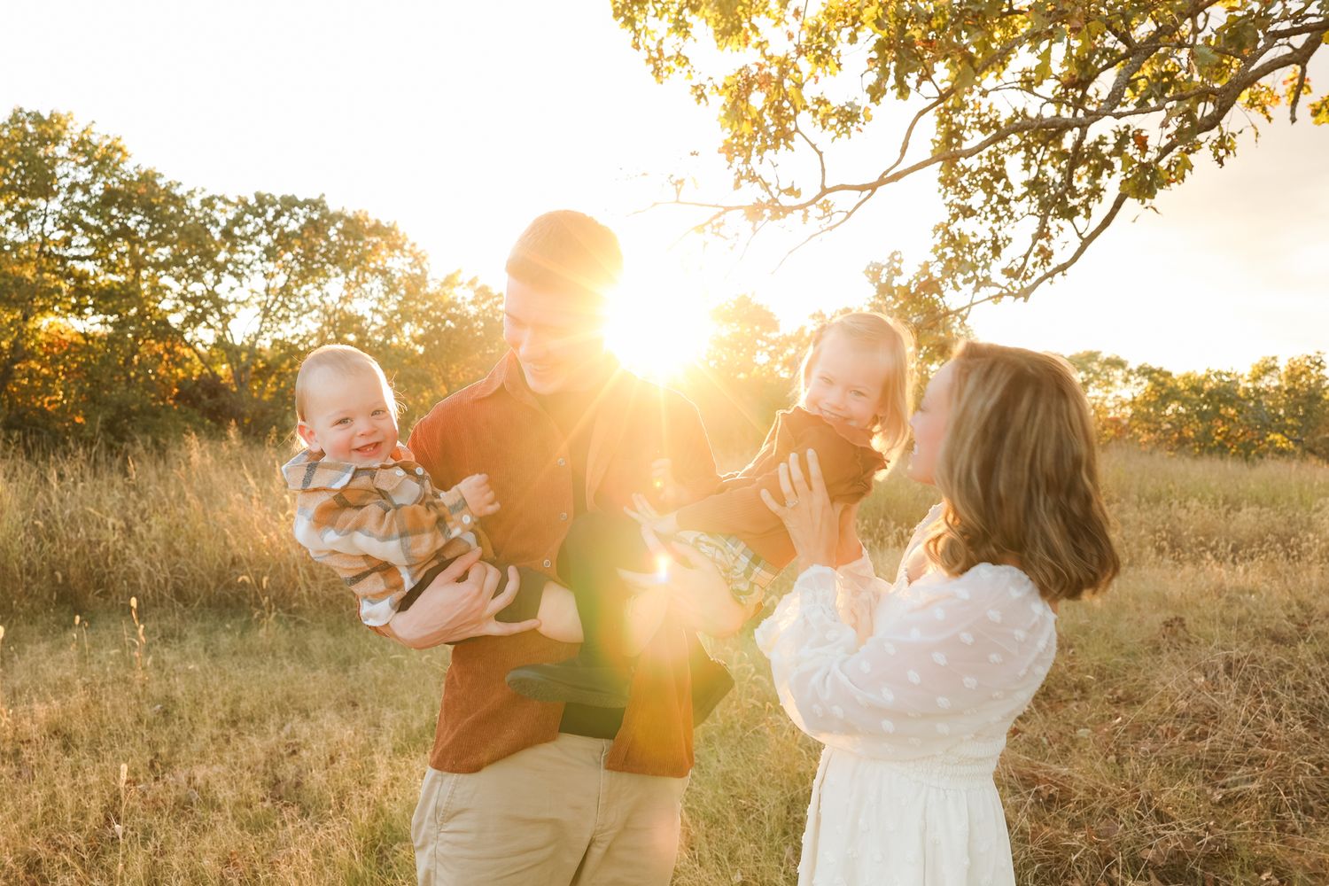 Family sharing playful moments together in a golden field during sunset.