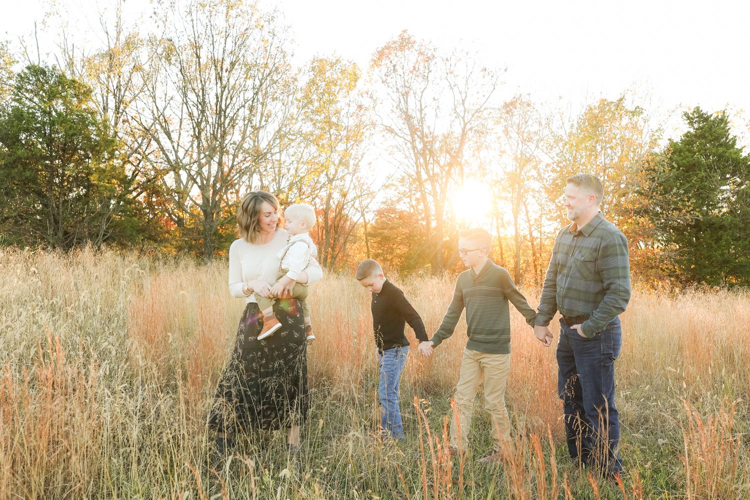 A family holds hands in a line while standing in tall grass at sunset.