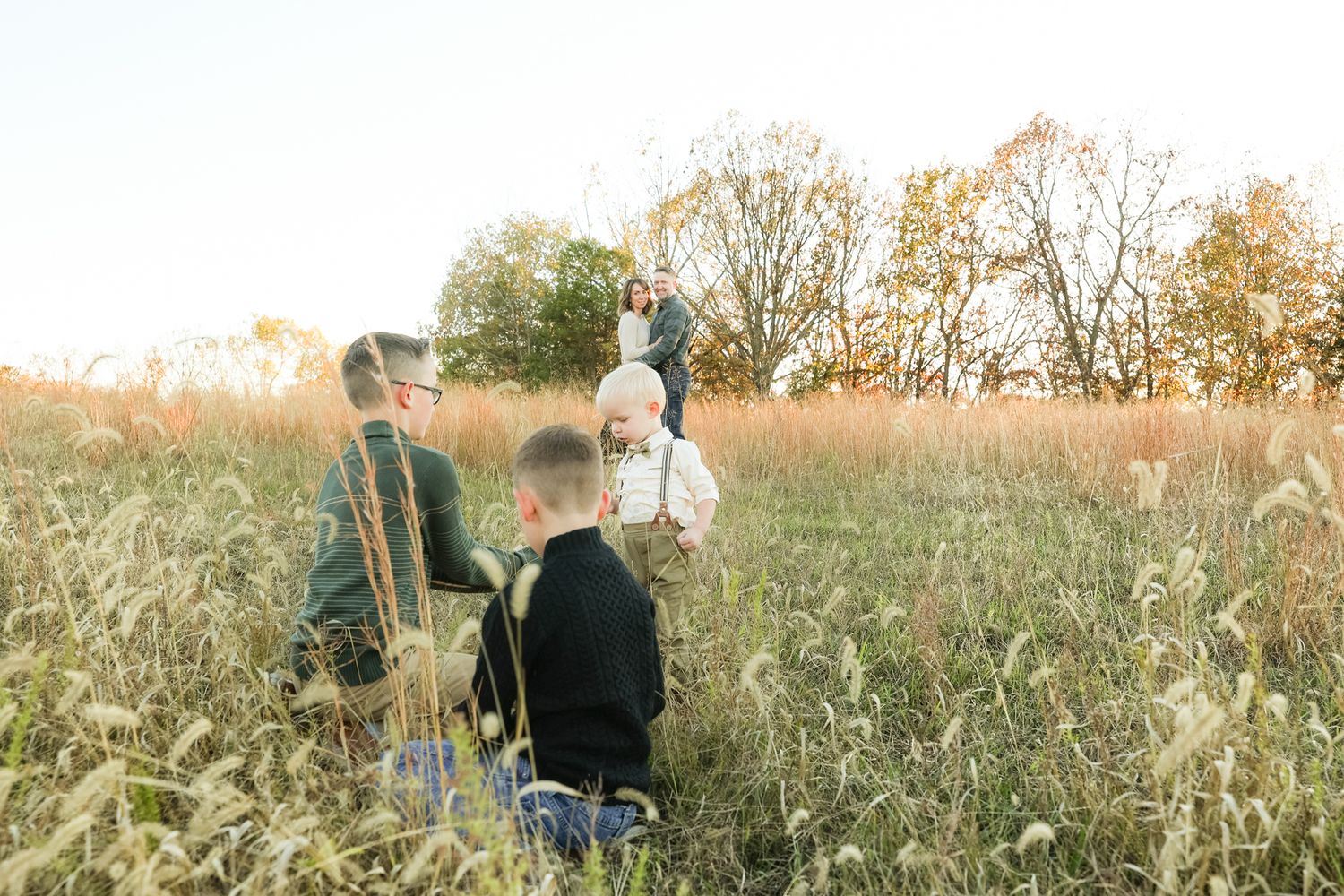 Family stands in tall grass field during golden hour photo shoot.