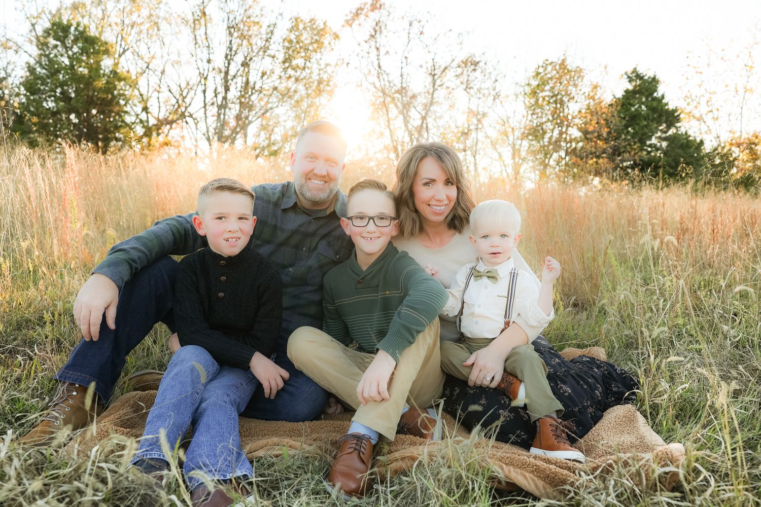 Family sits together in golden grass field during sunset portrait session.