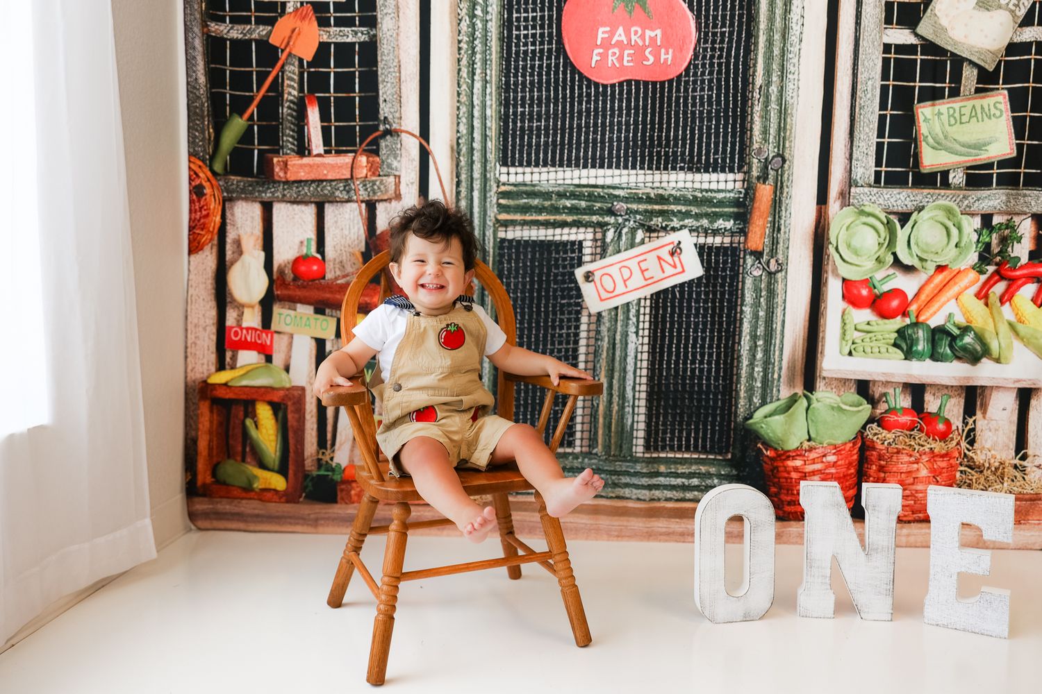 Child sitting on wooden chair with farm-themed first birthday party decorations.