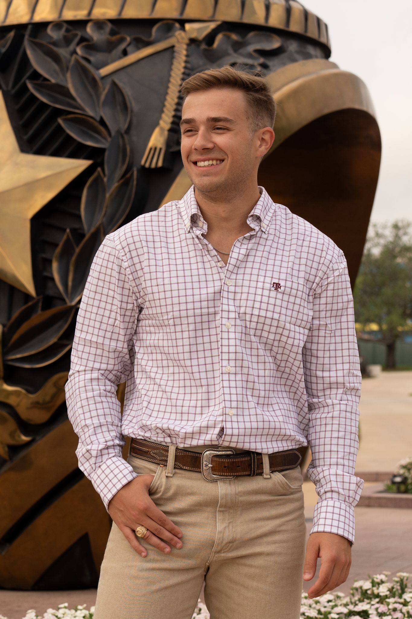 Student in checkered shirt poses by large decorative campus sculpture.