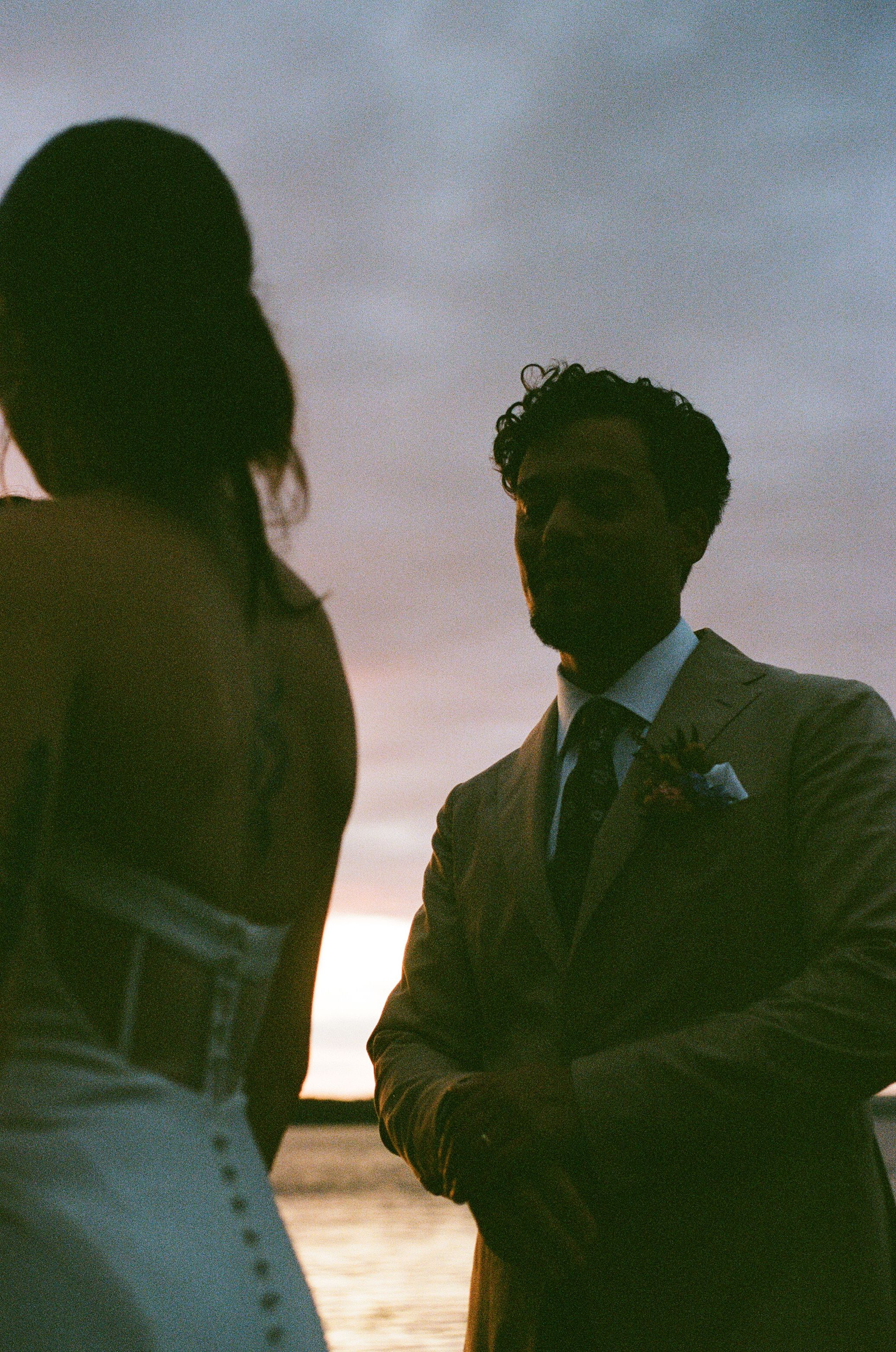 Romantic silhouette of newlyweds against a sunset sky during an outdoor wedding ceremony.