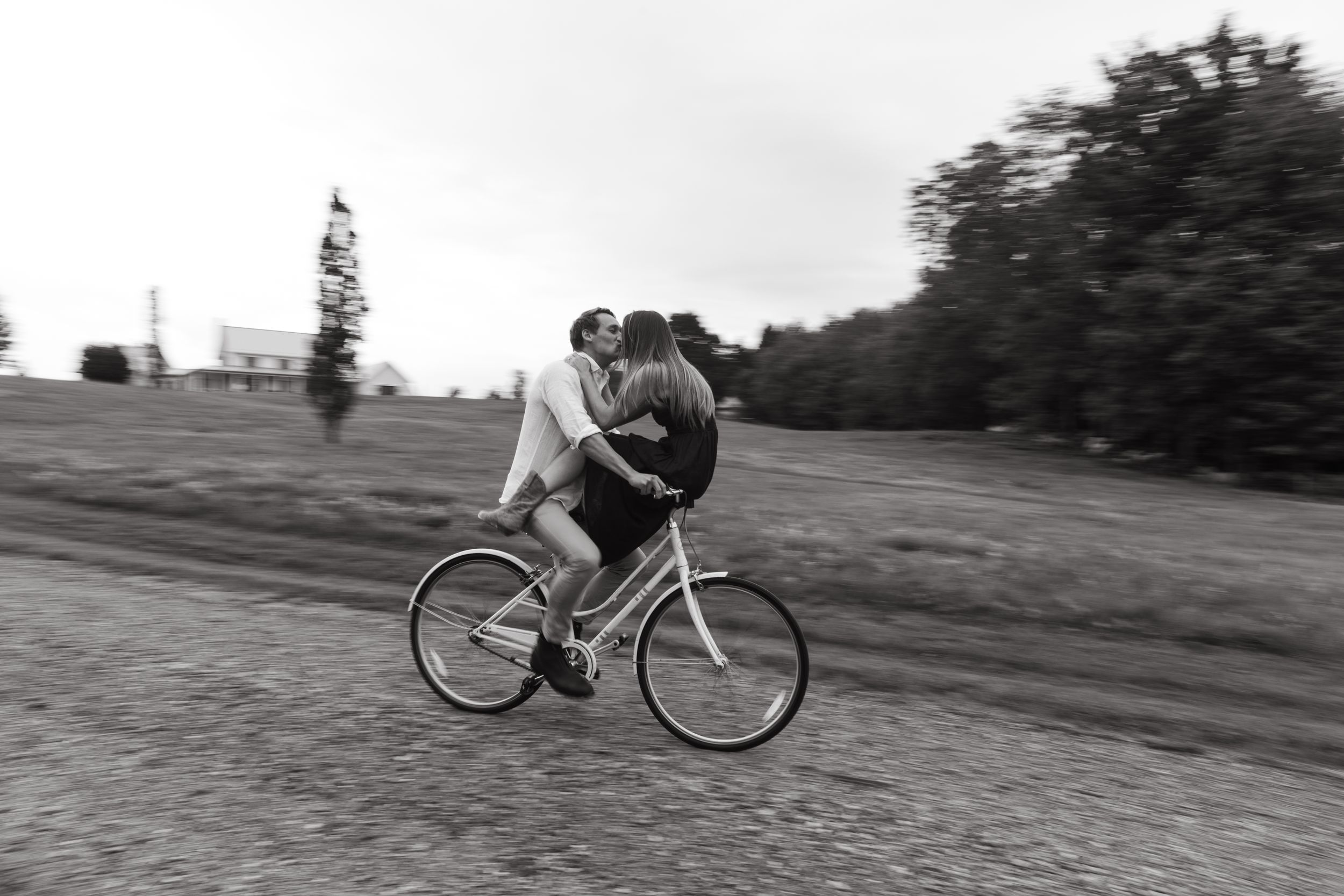 Playful couple riding together on bicycle in black and white motion shot.