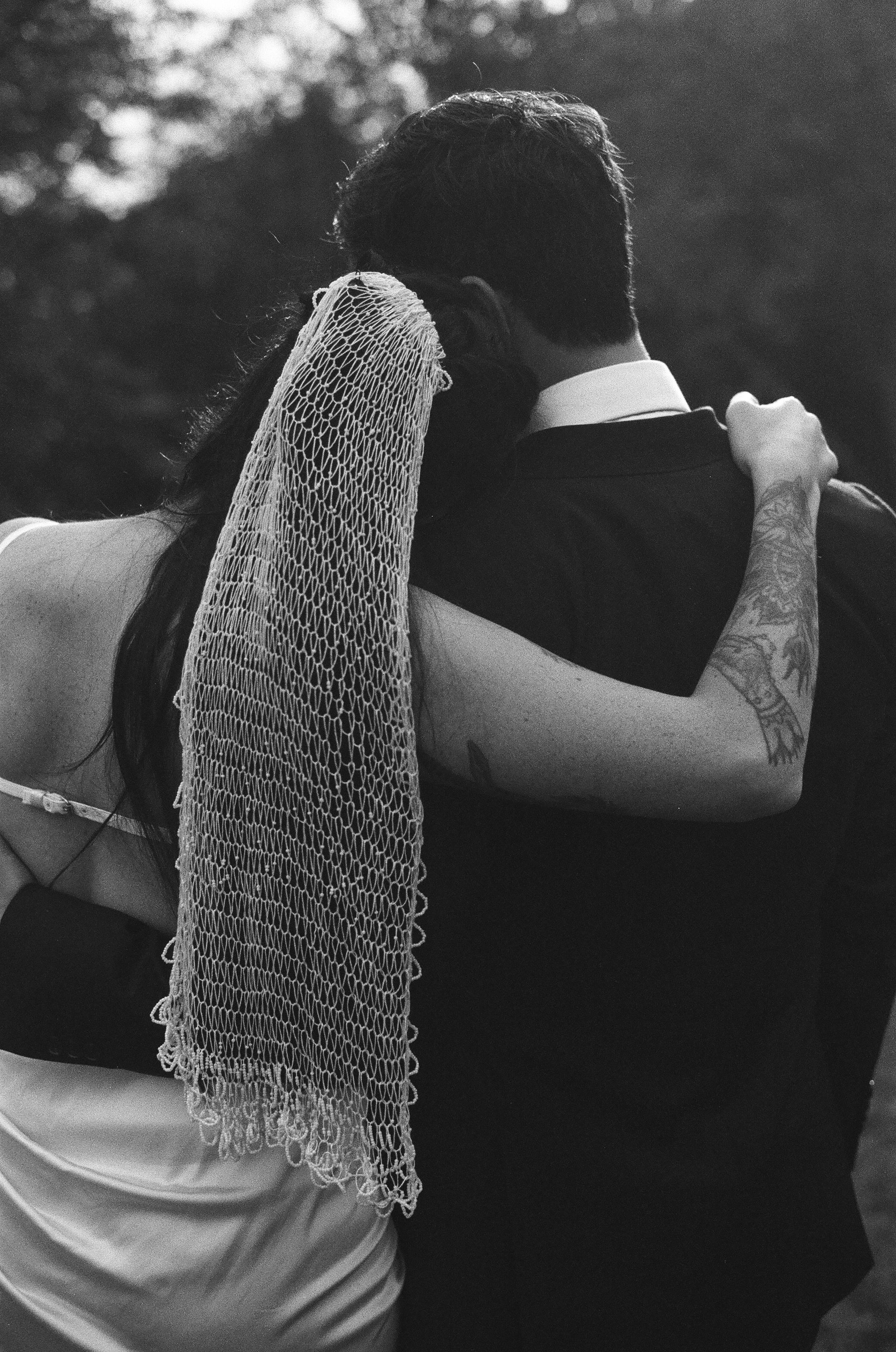 A black and white photo of a couple dancing together, with a delicate lace veil draping over their embrace.