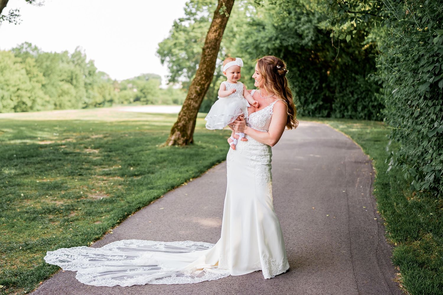 Long white bridal gown with flowing train photographed on a curved garden path surrounded by lush greenery.