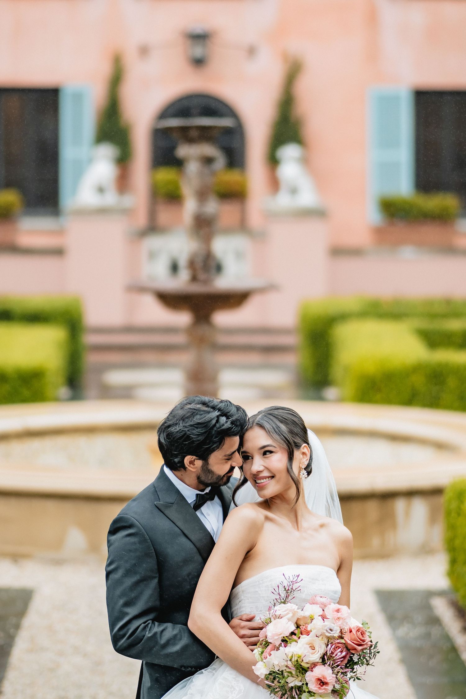 Elegant wedding photography at a Mediterranean style venue with pink walls and formal gardens surrounding a fountain.
