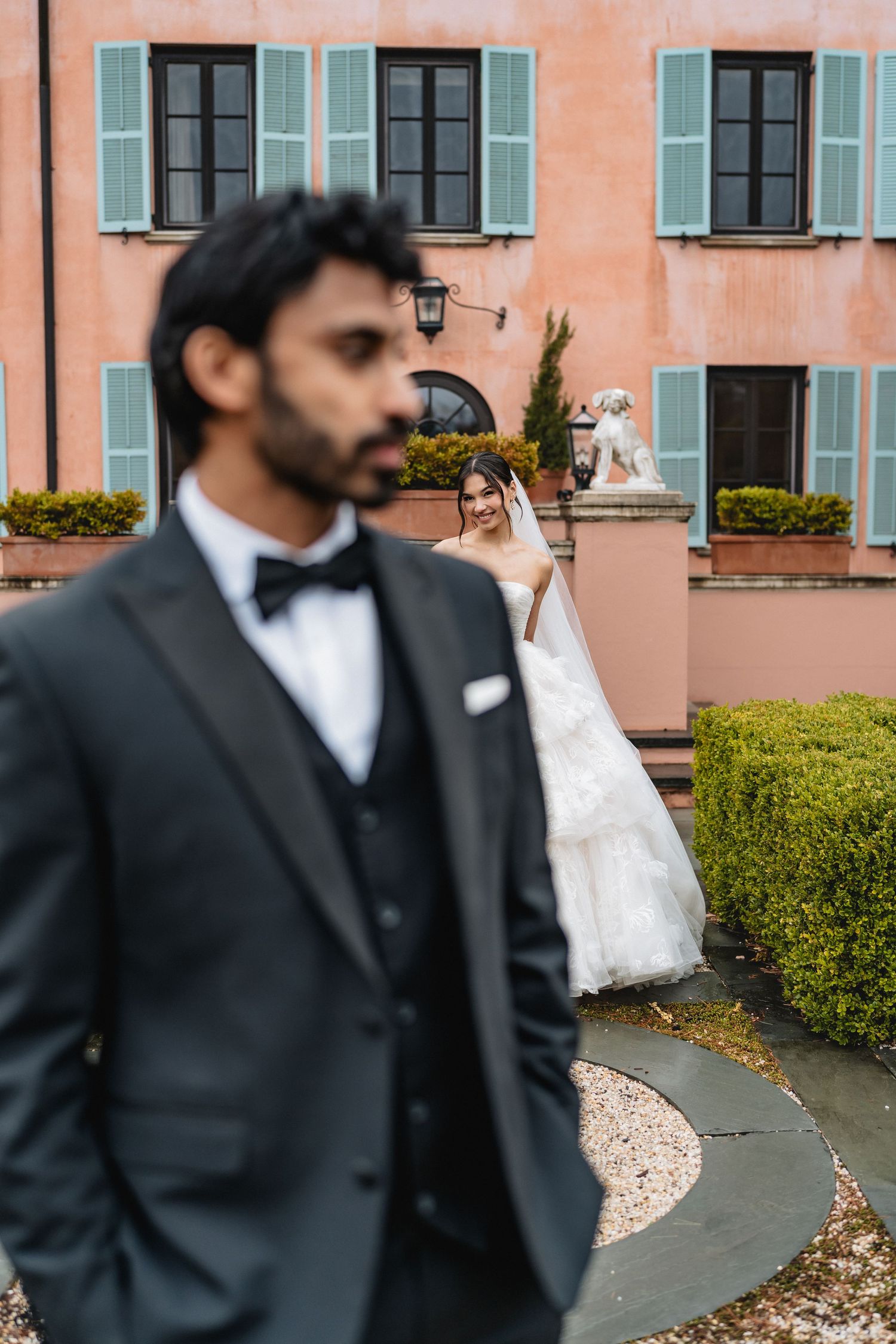 Artistic composition of wedding couple against pink building facade with blue shuttered windows.