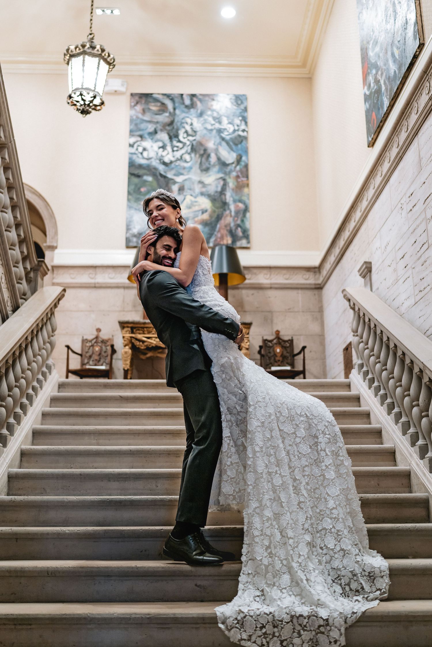 A romantic wedding moment on an elegant marble staircase with a white lace gown flowing down the steps.