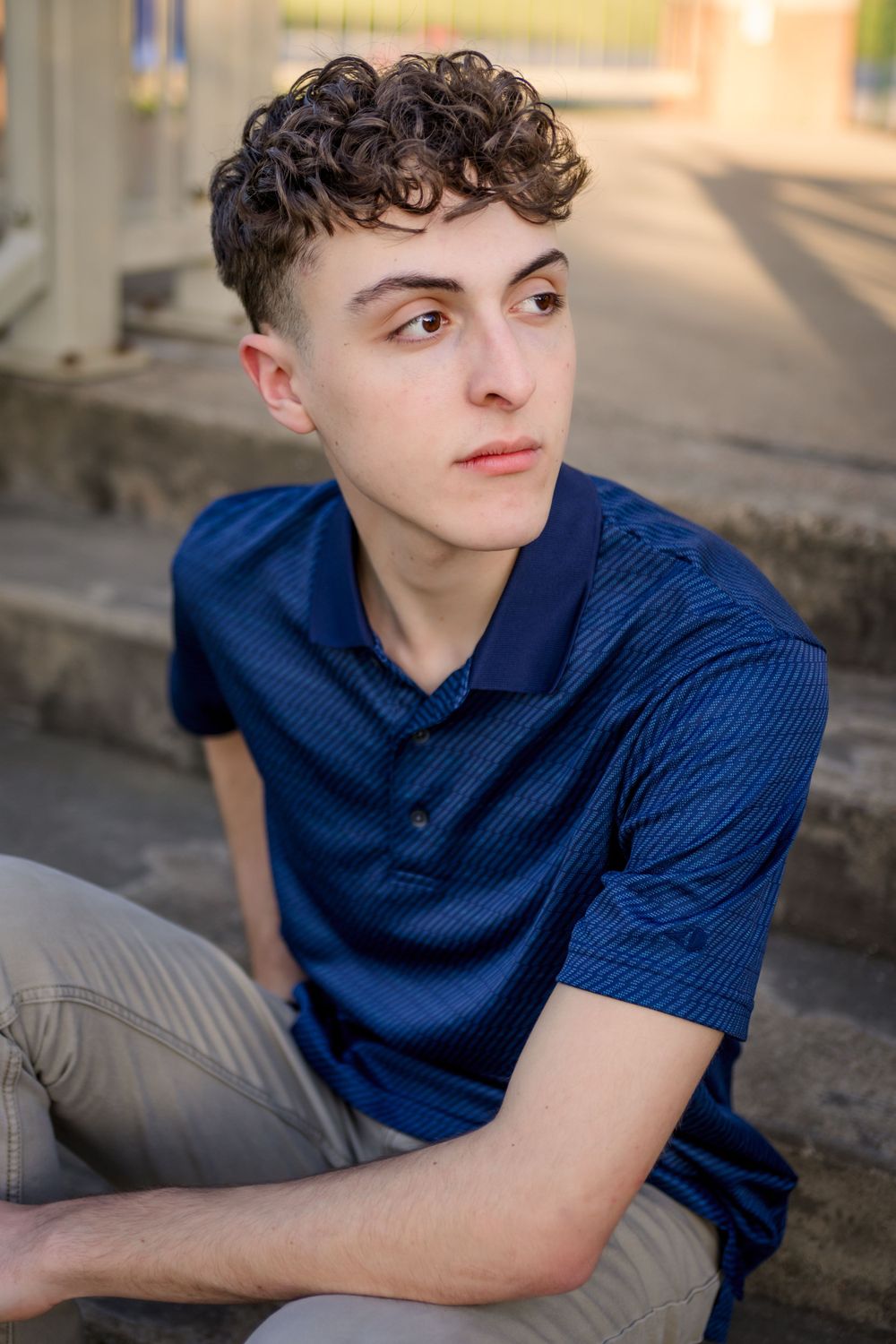 Portrait of person wearing navy blue polo shirt and khaki pants sitting outdoors in warm lighting.