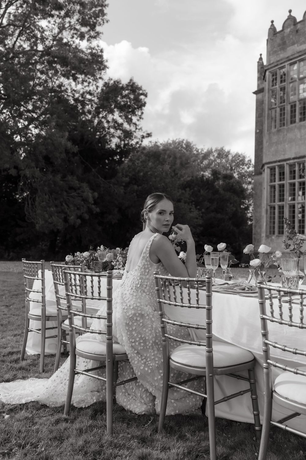 Black and white photo of an elegant outdoor wedding reception setup with Chiavari chairs and white tablecloths at a grand estate.