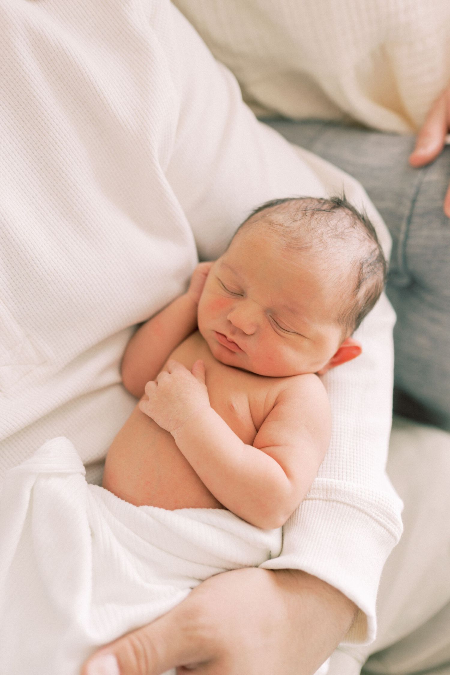 A peaceful newborn baby sleeping on soft white blankets during a gentle portrait session.