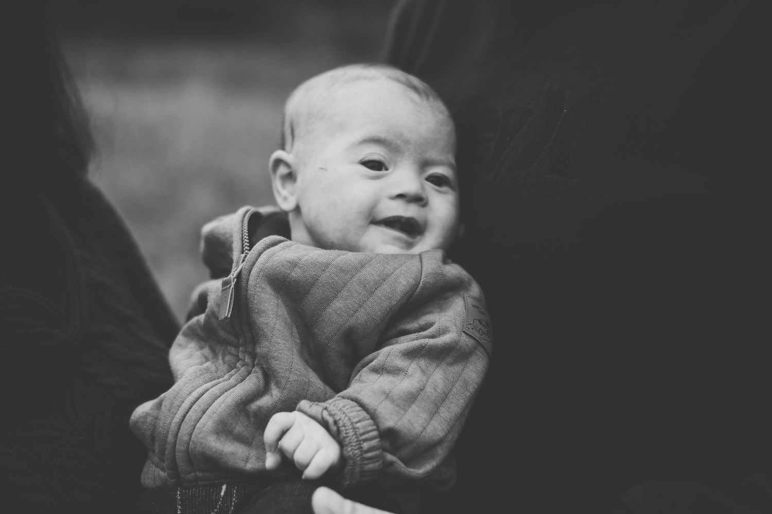 Black and white portrait of a joyful baby wearing a cozy sweater and smiling brightly.
