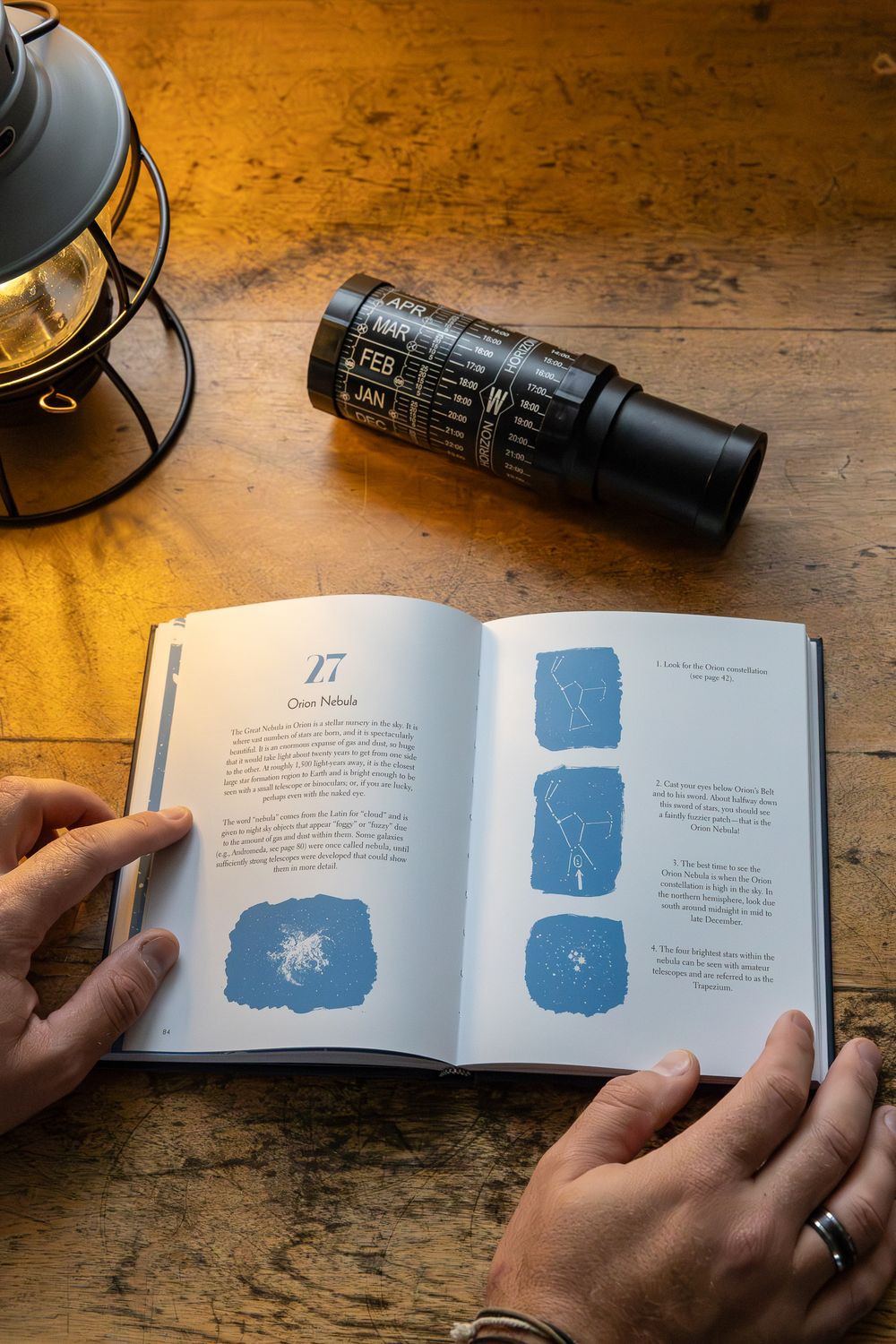 Open book with blue illustrations and lantern on wooden surface with hands holding pages.