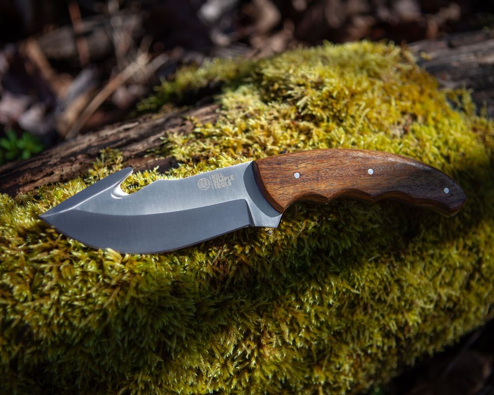 A hunting knife with wooden handle rests on green moss in natural lighting.