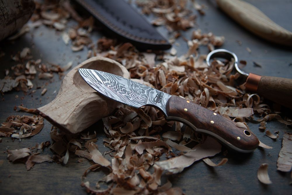A handcrafted knife with wooden handle surrounded by wood shavings on dark surface.