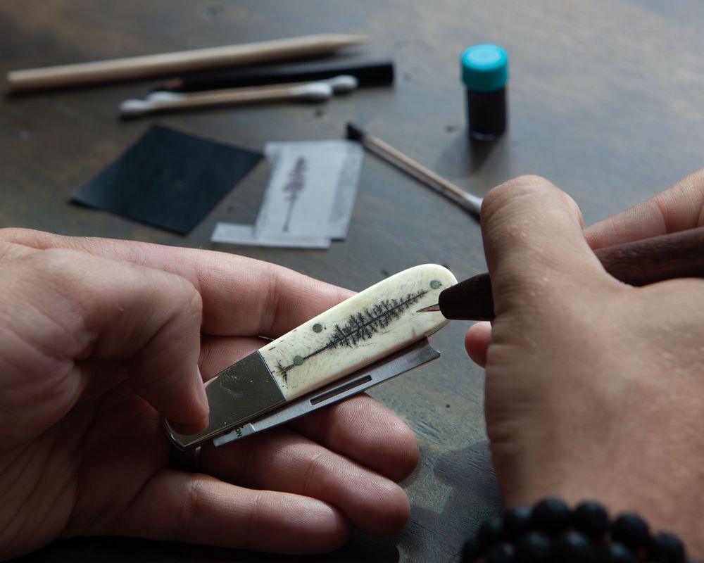 Hands carefully carving details into a wooden handle with precision tools.