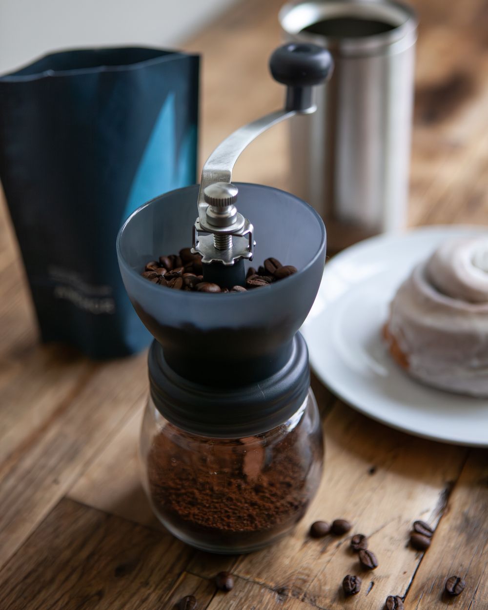 Manual coffee grinder with fresh beans being prepared on wooden table.