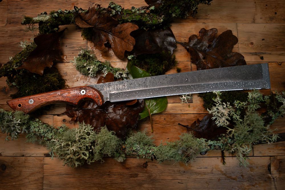 A rustic machete with decorative etching displayed on wooden surface with moss and foliage.