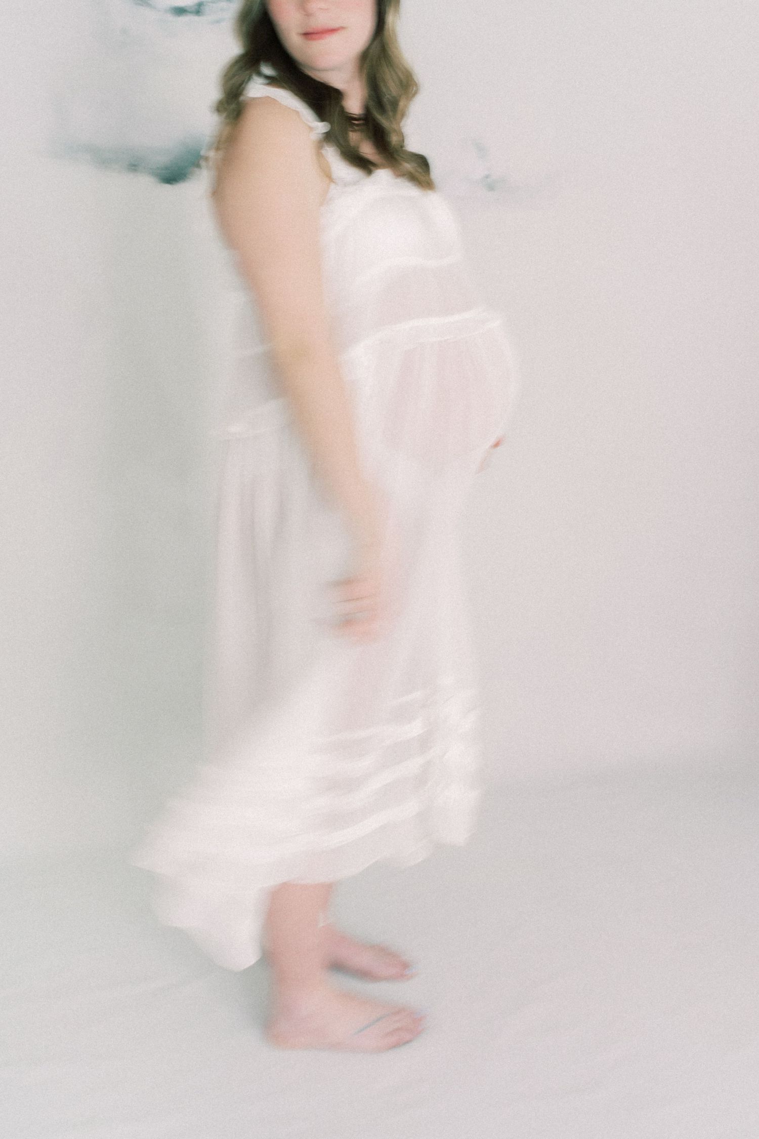 Ethereal white dress silhouette photographed with dreamy soft focus showing bare feet against light background.