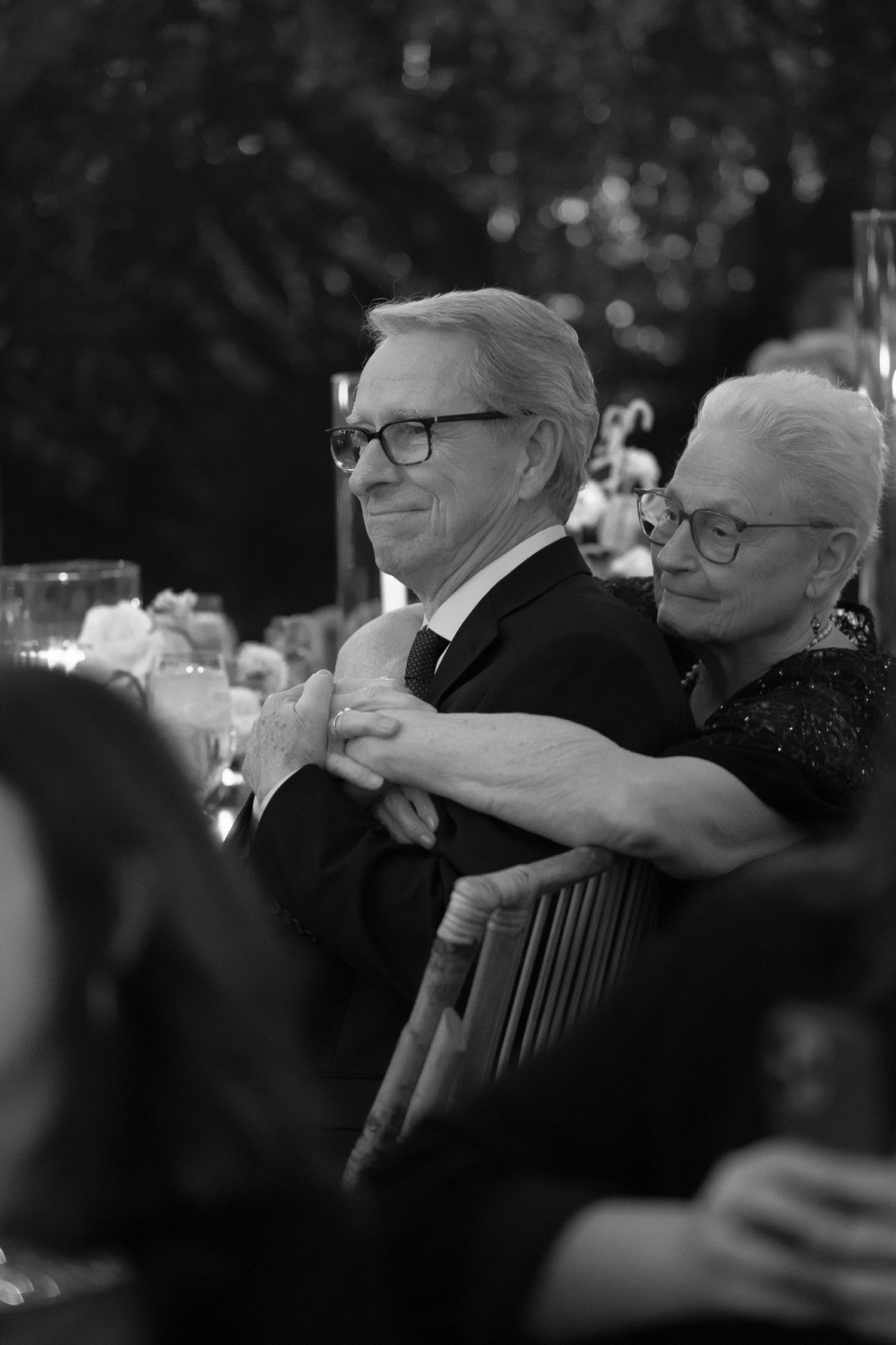 An elegant black and white photo of a couple at a formal dinner wearing glasses and formal attire.