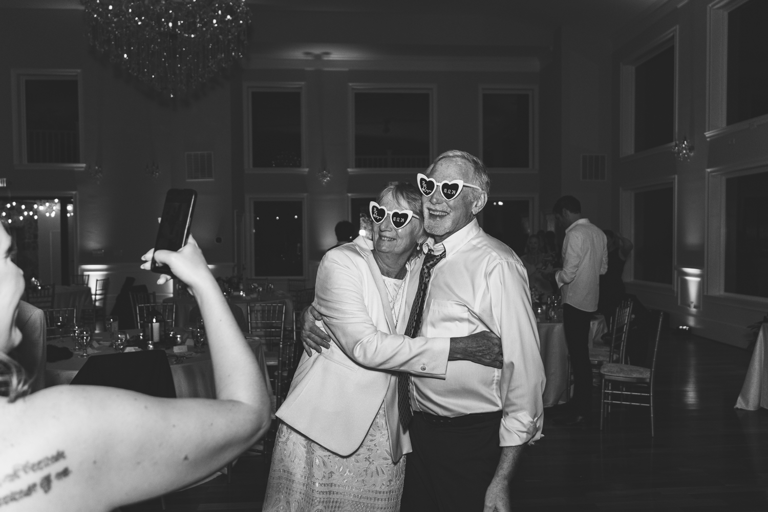 Black and white photo of wedding guests dancing with sunglasses at an indoor reception.