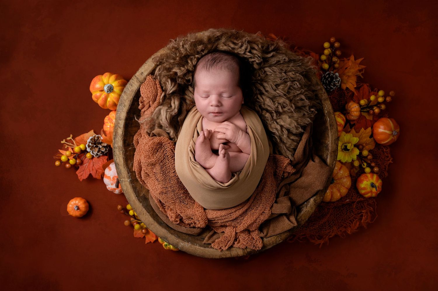 Newborn baby sleeping in basket with autumn decorations and orange pumpkins.