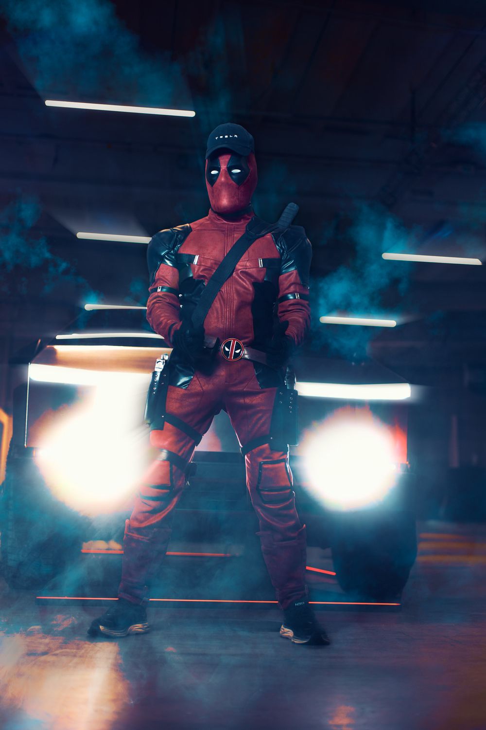 Deadpool cosplayer strikes action pose in dramatic lighting with glowing white lights and blue smoke effects.