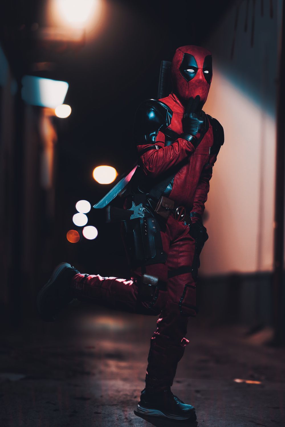 Deadpool cosplayer crouches in dimly lit hallway with bokeh lighting effects in dark atmosphere.