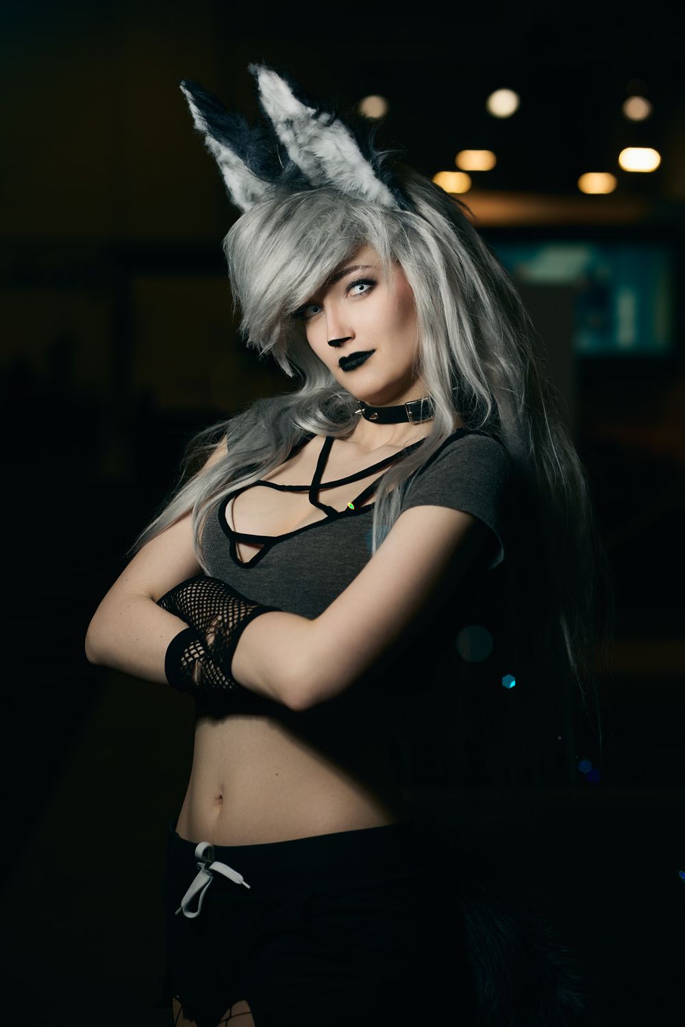 Gothic model in black mesh top and silver hair poses dramatically in moody dark setting.