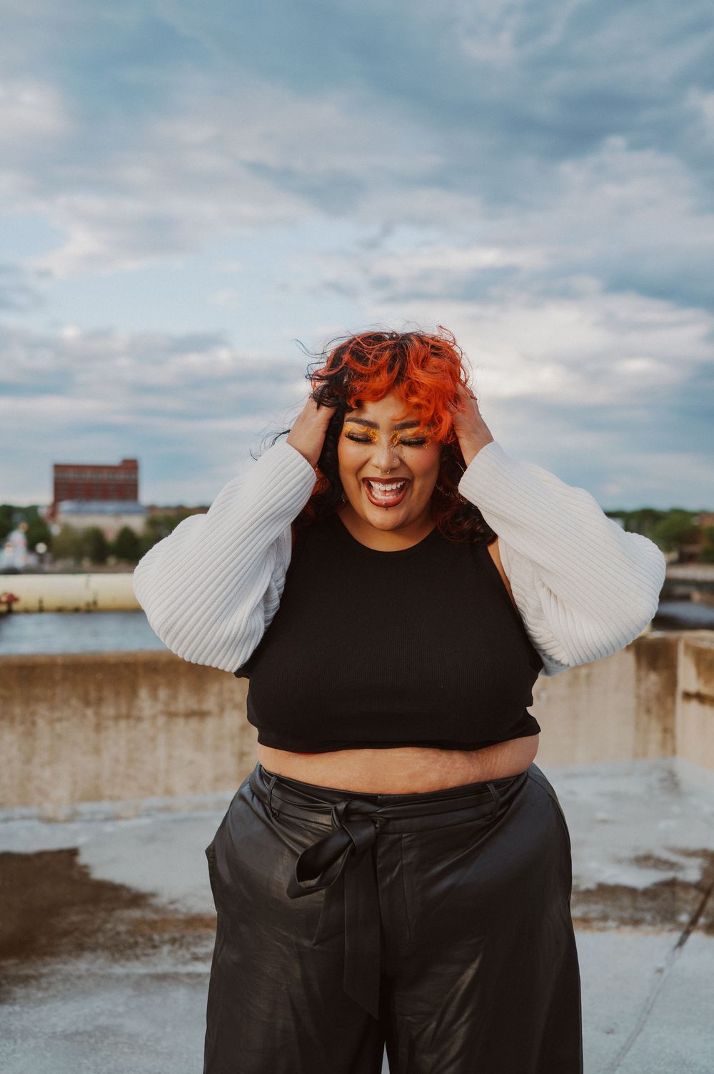 A person in black clothing laughs joyfully in a series of photos against a cloudy sky by the shore.