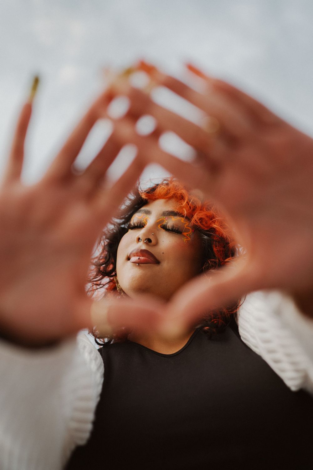 Artistic portrait shot through spread fingers showing a person with closed eyes in warm lighting.