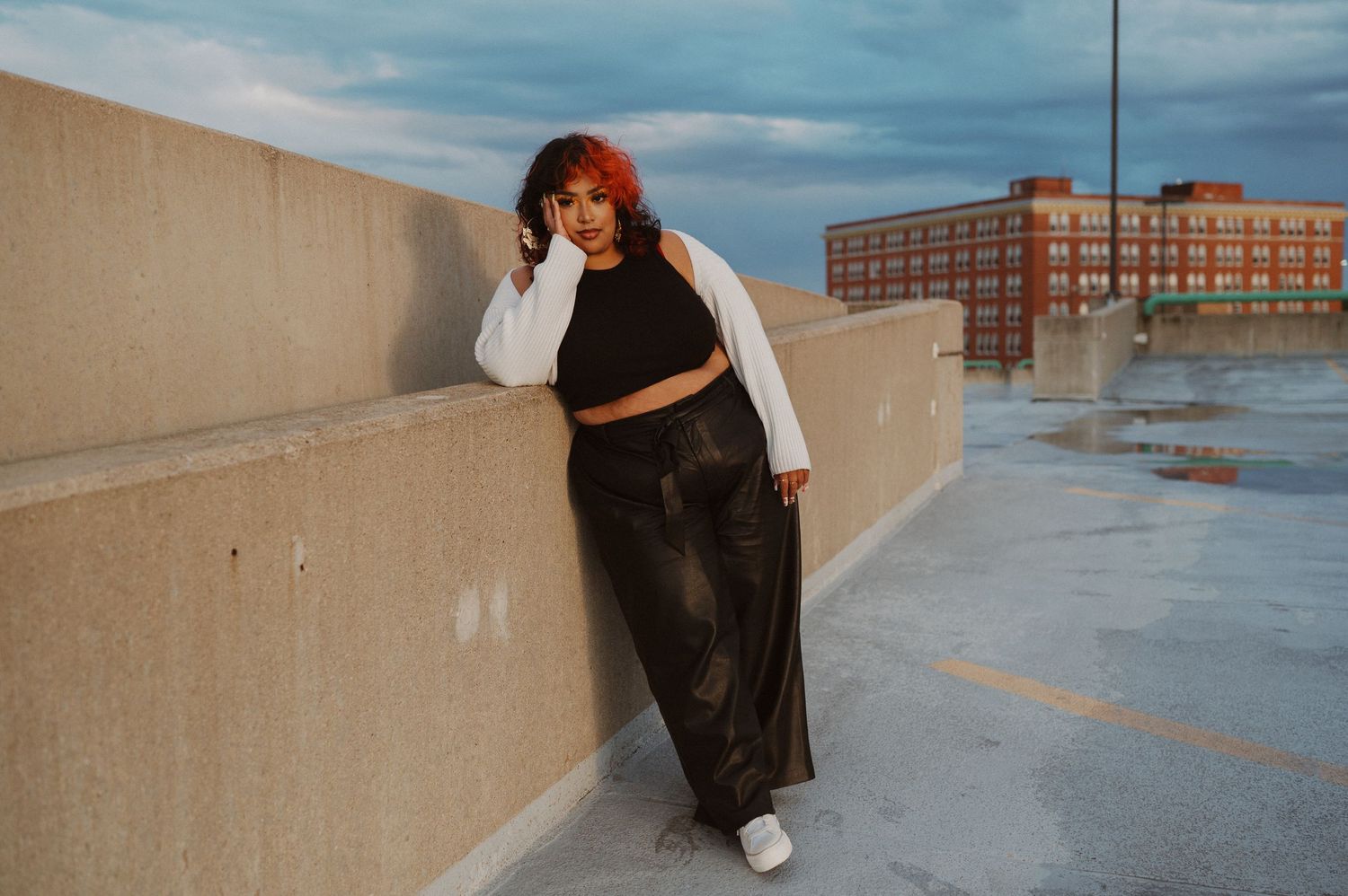 A person wearing black clothing strikes a dynamic pose against an urban rooftop with cloudy sky backdrop.