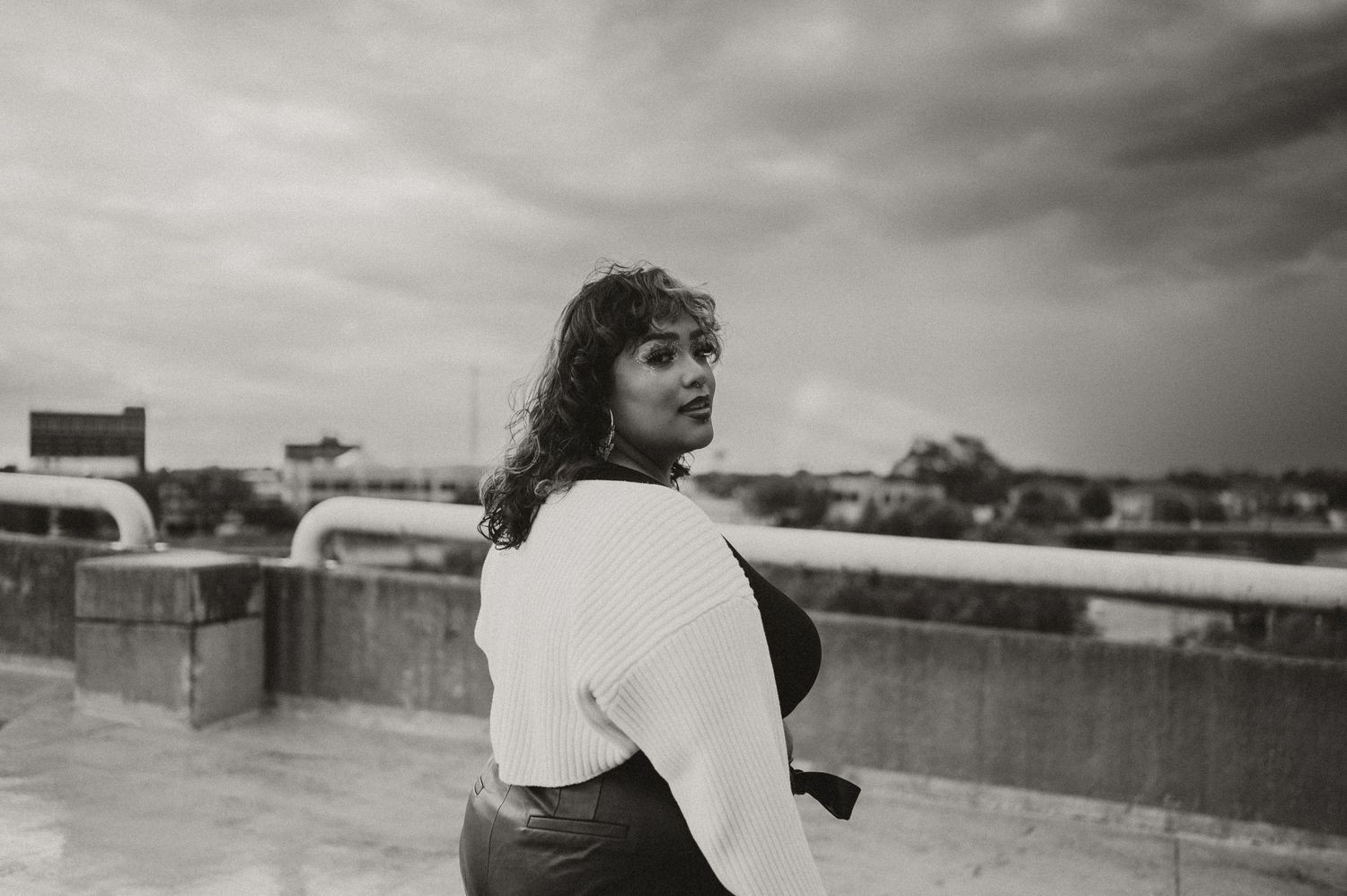 A black and white vintage photograph of a person on a rooftop looking back at the camera in an urban setting.