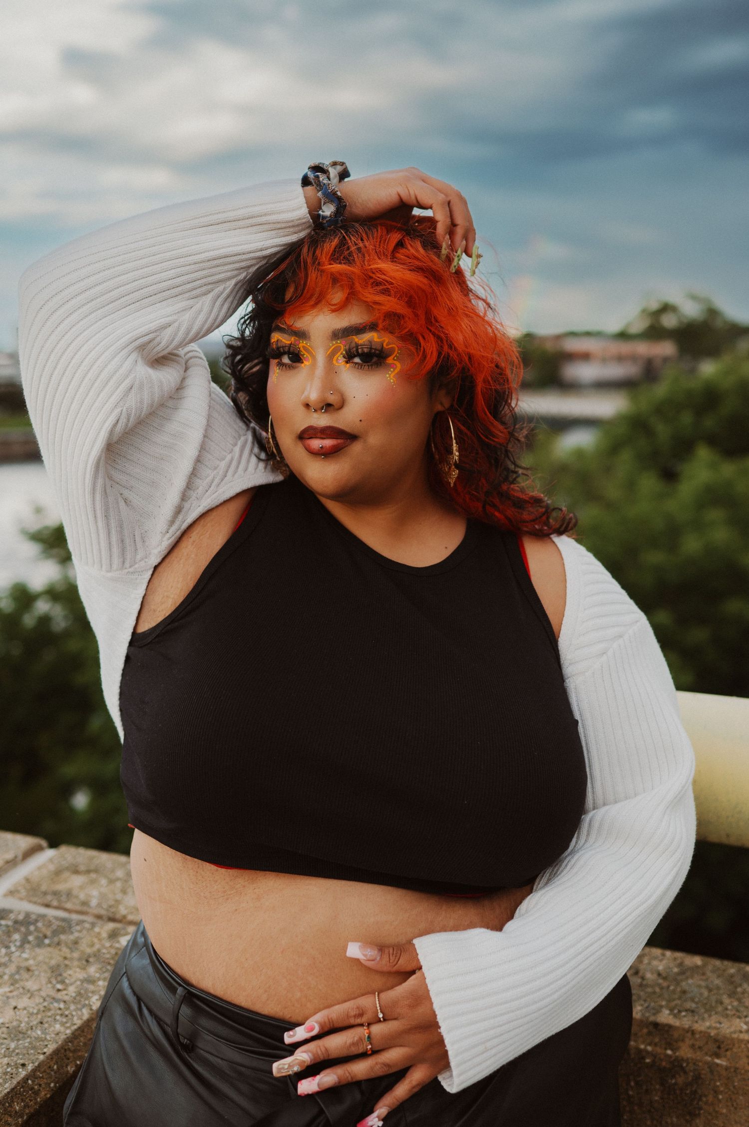 Outdoor fashion portrait with black crop top, white bell sleeves and vibrant red hair against cloudy sky backdrop.