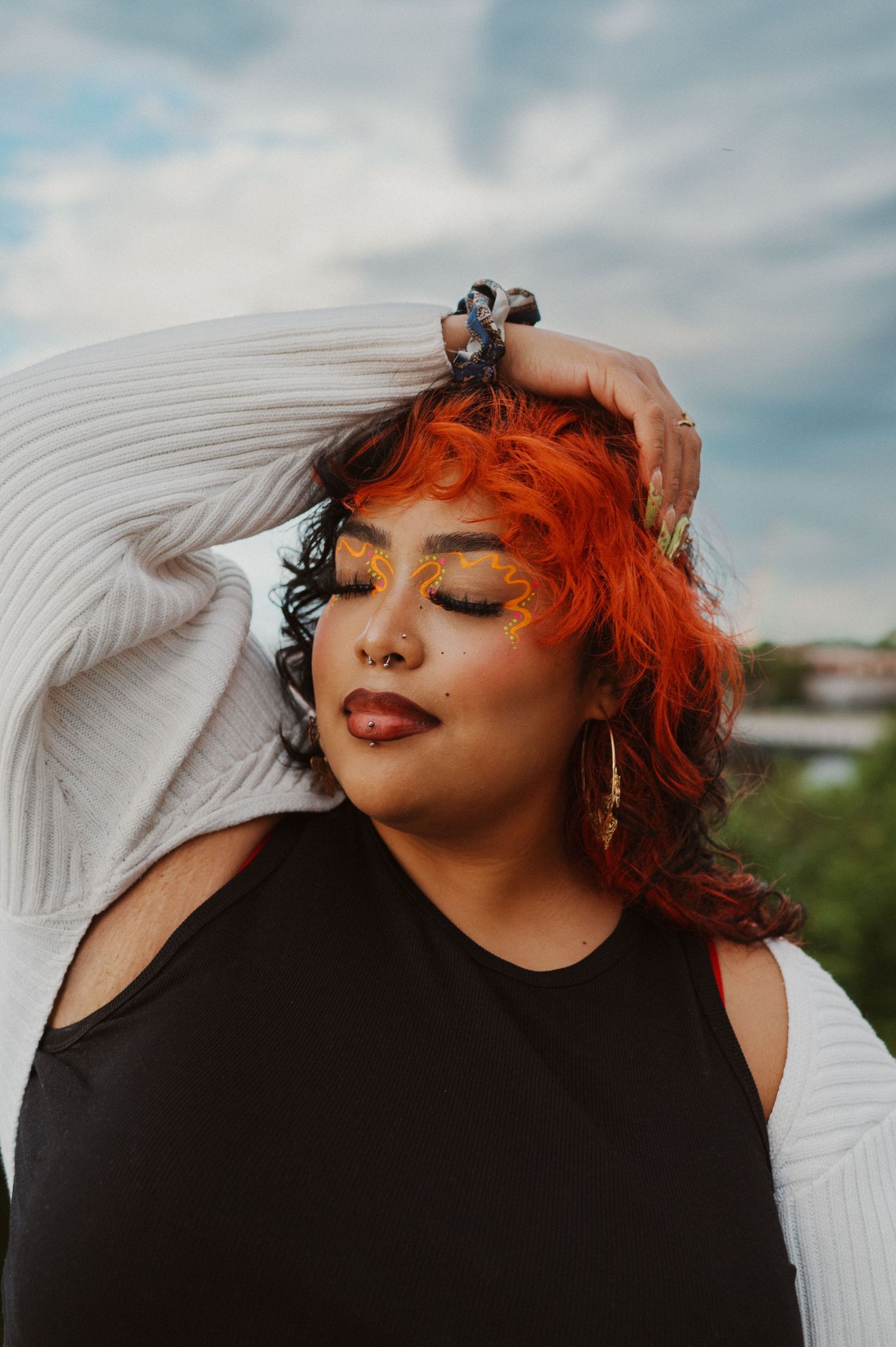 Fashion portrait of woman with bright orange hair wearing black top and white cardigan outdoors.
